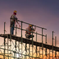 Man working on construction site with scaffold and building with sunset background,scaffolding for construction factory.