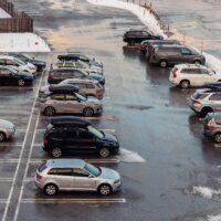 View from above on car parking with many vehicles and free lots at bright early frosty cold winter morning. Parking lot with snowdrifts near airport terminal or shopping business mall at cold weather.